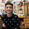 Sarah is sitting in a chair with her work desk behind her. She is smiling at the camera.