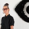 Susie is standing in front of her artwork. It is the same of an eye made out of plastic bags.