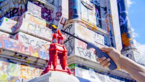 There is a small replica of the Robert E. Lee statue made out of wax. There is a wick where the head should be. A hand holding a lighter is outstretched and lighting the candle statue on fire. Behind the candle is the base of the real Robert E. Lee statue which is covered in graffiti.
