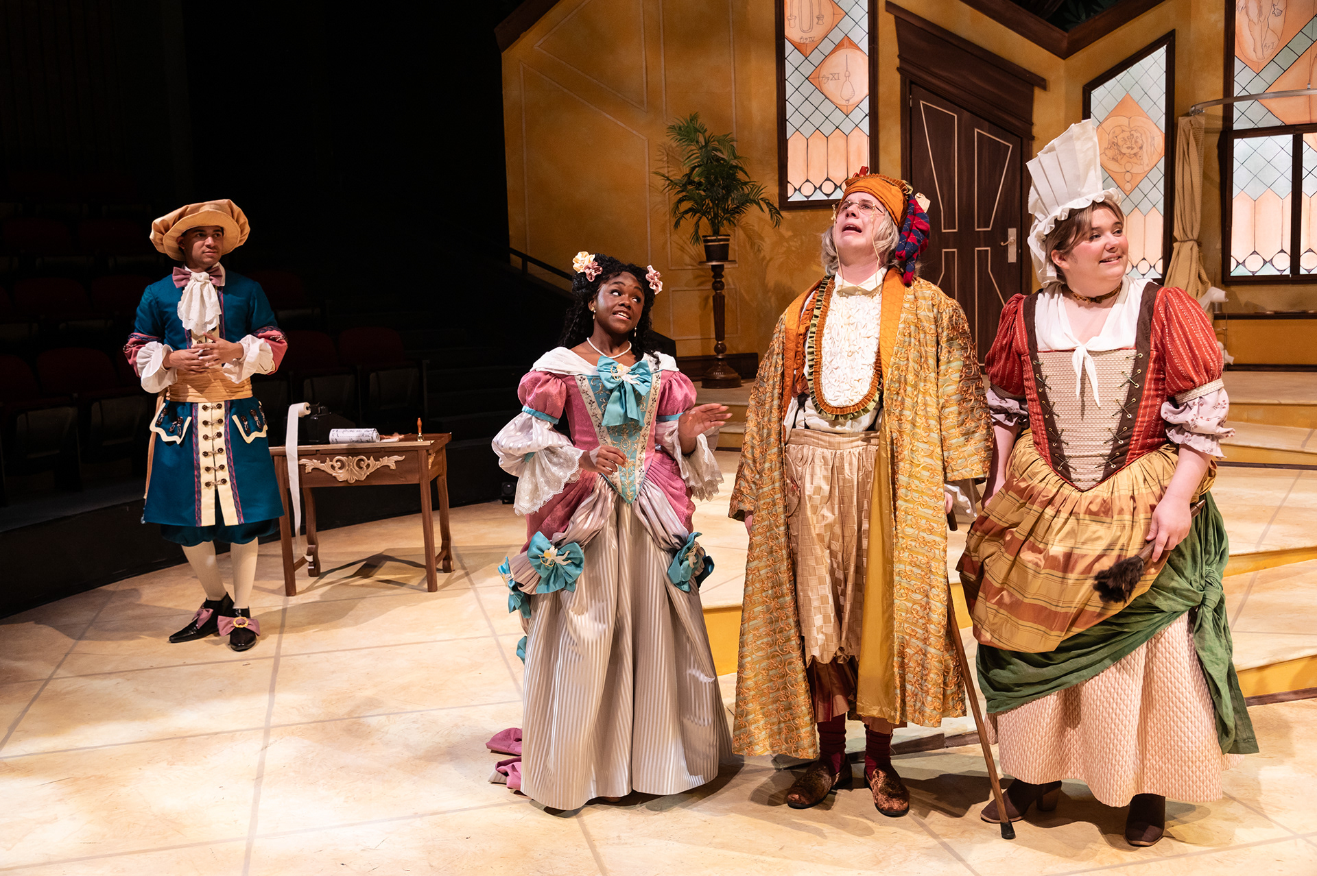 Performance photo of three actors in the foreground and one in the background in costume