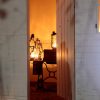 There is a white shed with its door open. Inside, there are three stretched gas lamps glowing in a dark room. There are on top of an old table and a box. On the exterior of the shed, above the doorframe, is "05/01" writing in charcoal.  