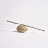 A small sculpture sits on the ground. The sculpture is made up of a rock with a long stick balancing on top. Very thin beige thread is wrapped around the stick from one end to the other.