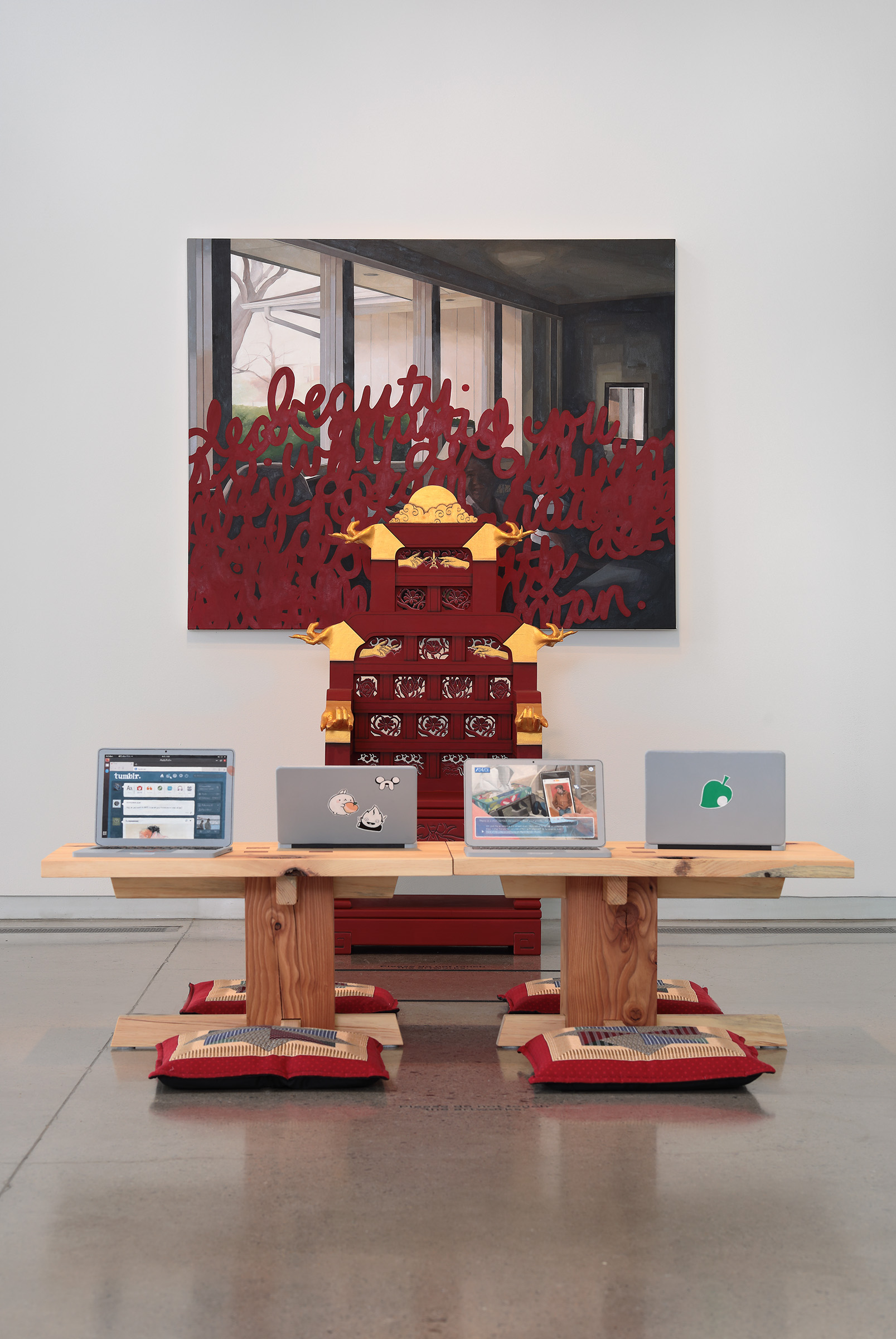A table with four monitors sits in a gallery space with a painting