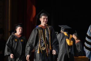 graduates in regalia crossing the stage at commencement