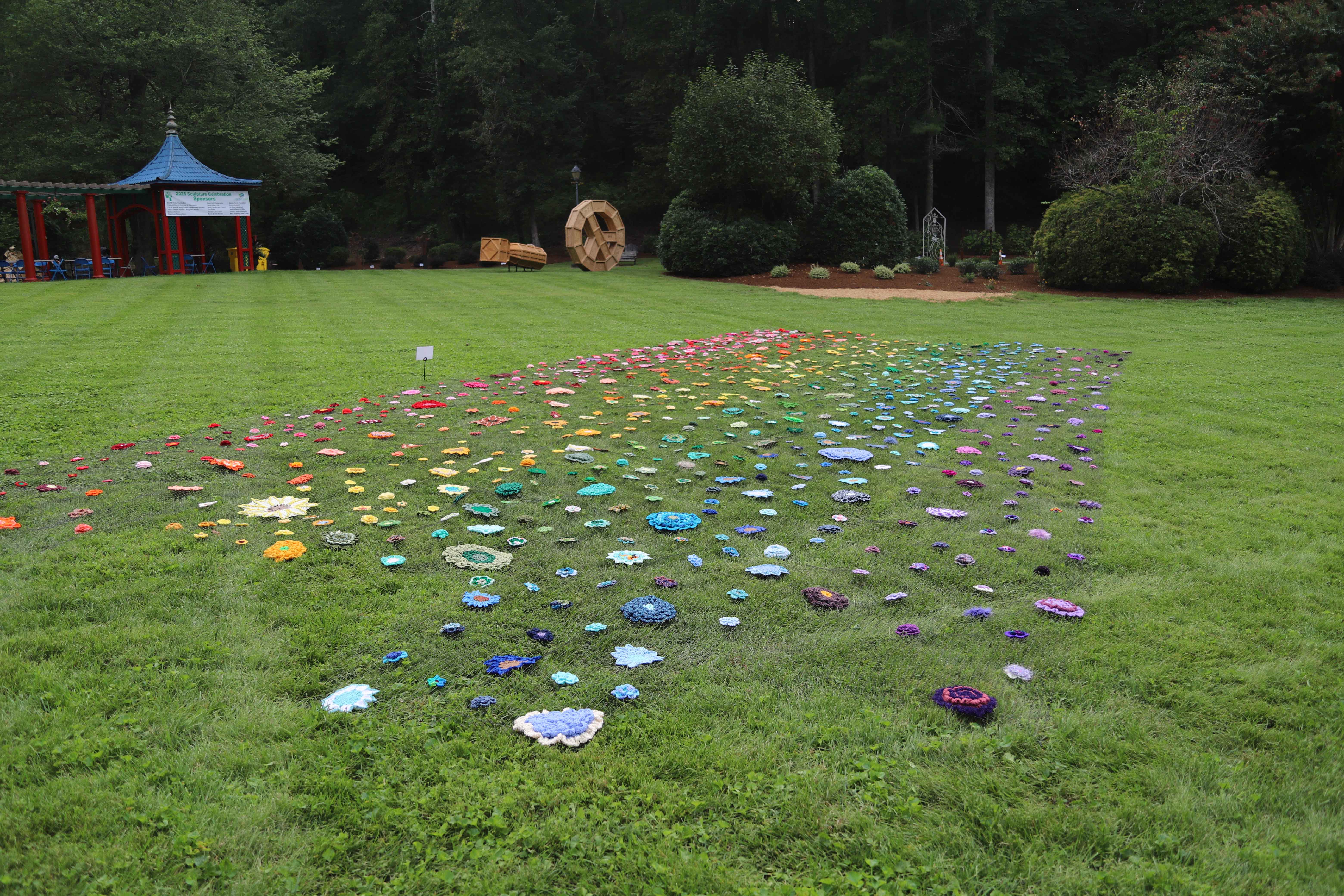 A large assortment of crocheted flowers in lay on the grass, seperated in color sections of the rainbow.