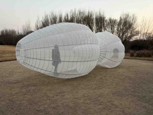 Kendall Buster's sculpture, two linked orbs made of metal frame and transparent white cloth. A person stands inside the sculpture.