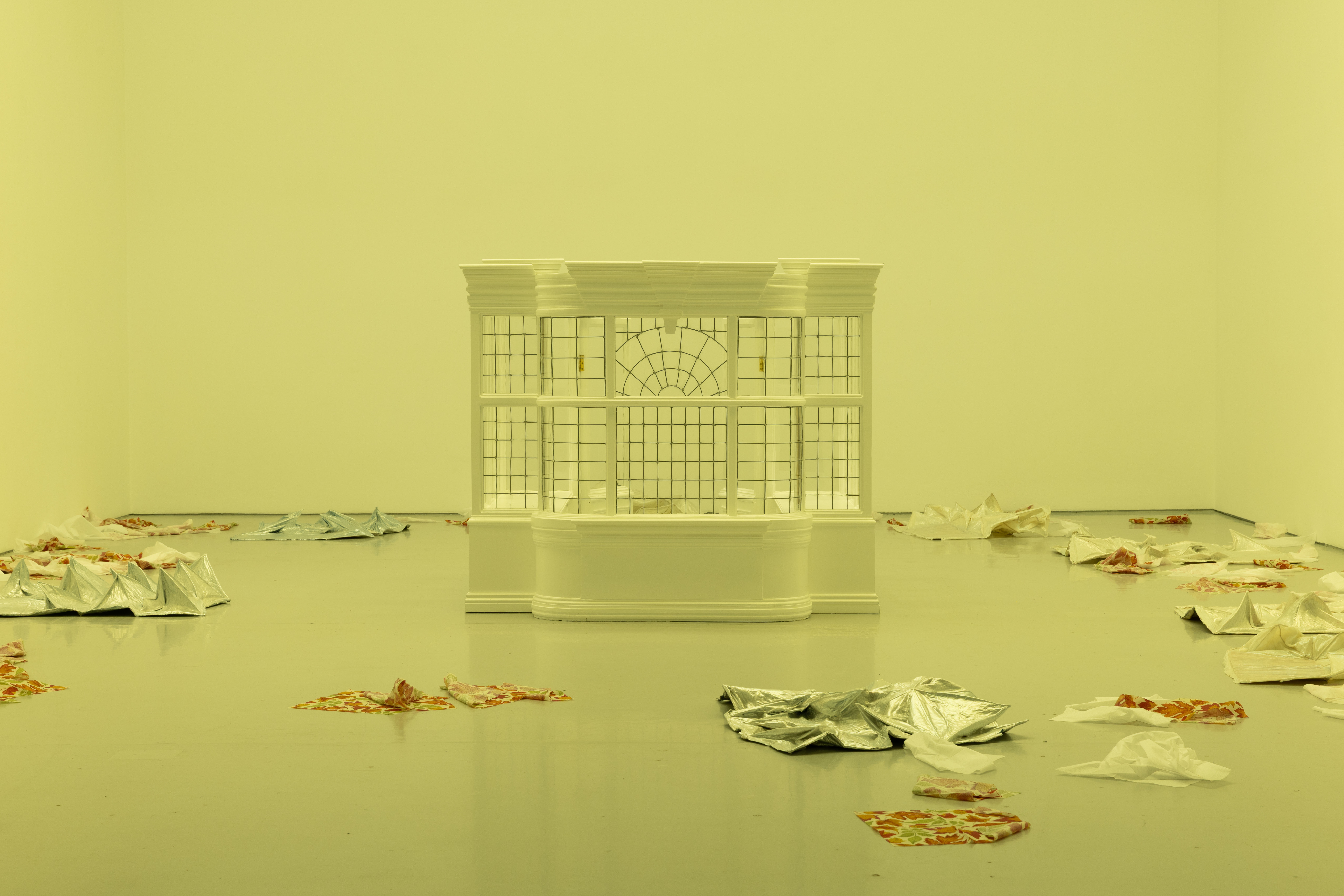 A the exterior section of a house's sunroom stands in the center of an empty room. The floor of the room has small piles of fabric pieces.