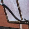 A water hose is attached to the ceiling and falling out an open window. Water drops are leaking from the center of the hose.